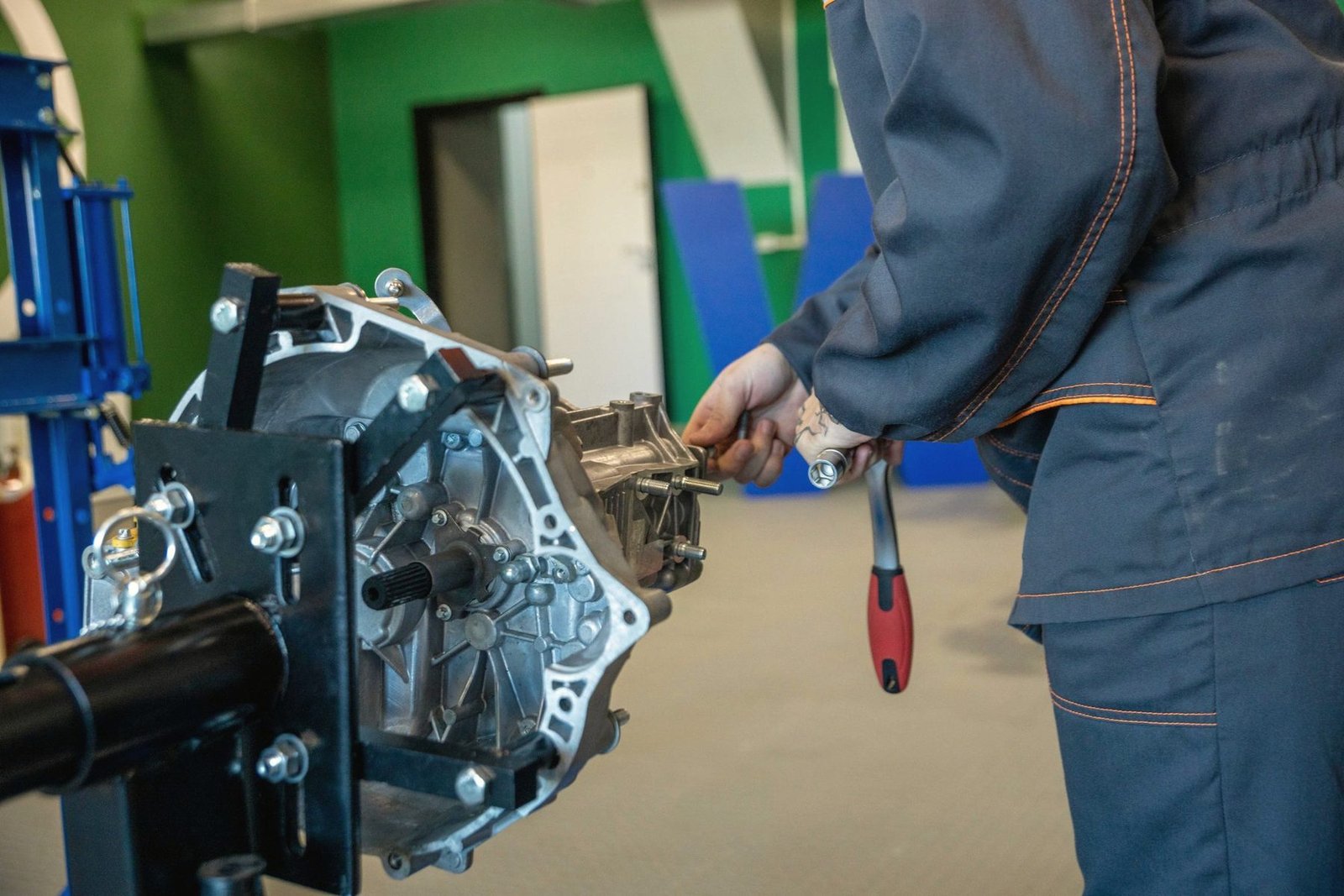 A transmission bolted to a repair stand while a mechanic works on it with a hand tool