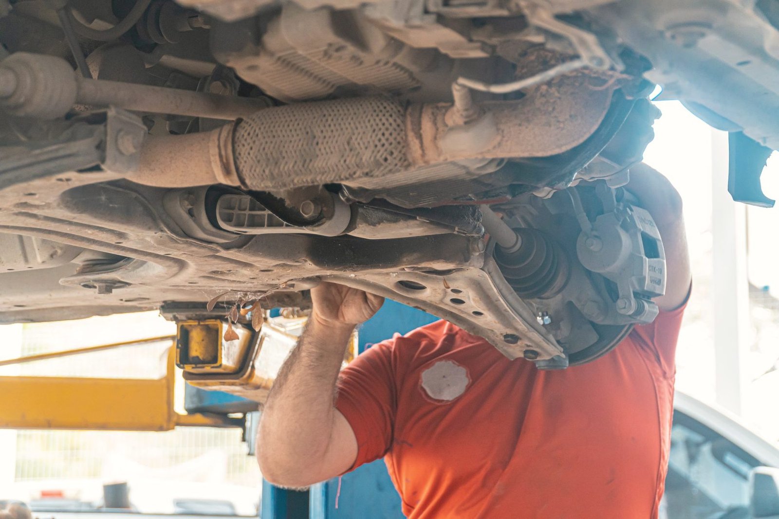 A mechanic standing under a raised car inspecting the drivetrain